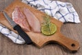 Knife on raw red mullet fillets laid on a cutting board with a slice of lemon and rosemary close-up on a wooden background