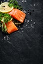 Fresh fish portions with lemon slices, rosemary, parsley, salt and peppercorns on a black stone background