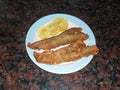 fresh fried floured hake fish fillets with lemon slices on a plate with a brown marble background