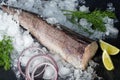 Fresh frozen hake carcass. Fish fillet with culinary ingredients, herbs, pepper, and lemon on a black background