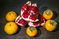 Kitchen still-life. Wholesome ripe fruits of pomegranate, mandarine and persimmon on a dark brown table. Royalty Free Stock Photo