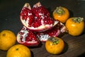 Kitchen still-life. Wholesome ripe fruits of pomegranate, mandarine and persimmon on a dark brown table. Royalty Free Stock Photo