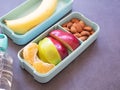 Fresh fruit in light green lunch box with almond, apple, orange, banana, water bottle on grey background. Take away food. Royalty Free Stock Photo