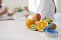 Fresh fruit and measuring tape on desk against blurred dietitian giving consultation to patient