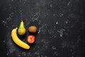Fresh fruits banana, pear, apple and kiwi on a black stone grunge background. Top view, flat lay. Minimal still life