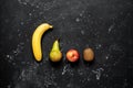 Fresh fruits banana pear apple and kiwi in a line on a black stone grunge background. Top view flat lay. Minimal still life