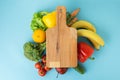 Fresh fruits and vegetables with blank wooden cutboard on the blue background. Mock up for healthy food concept Royalty Free Stock Photo