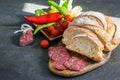 Fresh fuet and sliced homemade bread on the wooden cutting board, fresh vegetables on the dark background Royalty Free Stock Photo