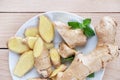 Fresh ginger root sliced and mint leaves on a white plate and a light wooden background. Royalty Free Stock Photo