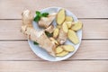 Fresh ginger root sliced and mint leaves on a white plate and a light wooden background. Royalty Free Stock Photo