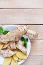 Fresh ginger root sliced and mint leaves on a white plate and a light wooden background. Royalty Free Stock Photo