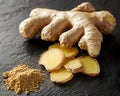 Fresh ginger root with sliced pieces and ground ginger powder on a dark stone surface, showcasing the natural textures and vibrant Royalty Free Stock Photo