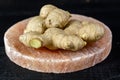 Fresh ginger roots on pink salt board close up on black wooden background