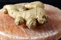 Fresh ginger roots on pink salt board close up on black wooden background