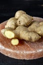 Fresh ginger roots on pink salt board close up on black wooden background