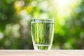 Fresh glass of drinking water on wooden tabletop on blurred green nature bokeh background