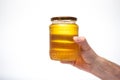 Fresh golden yellow bee honey in a glass jar, held by Caucasian male hand. Close up studio shot, isolated on white background Royalty Free Stock Photo