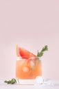 Fresh grapefruit juice with ice, piece and green rosemary closeup on soft white wood table and pink background, vertical. Royalty Free Stock Photo