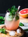 Fresh grapefruit and mint homemade lemonade with ice in glass on wood board. Summer drink with citrus and herbs