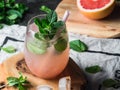 Fresh grapefruit and mint homemade lemonade with ice in glass on wood board. Summer drink with citrus and herbs