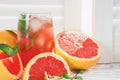 Fresh grapefruits and glass of grapefruit juice with ice and mint on rustic white wooden table opposite the blinds with copy space Royalty Free Stock Photo