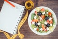 Fresh greek salad with feta cheese and tape measure with notepad for notes. Slimming and healthy nutrition Royalty Free Stock Photo