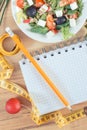 Fresh greek salad with feta cheese and tape measure with notepad for notes. Slimming and healthy nutrition Royalty Free Stock Photo