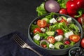 Fresh greek salad with olives, feta cheese, tomato, cucumber, onion with fork on towel on black background