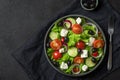 Fresh greek salad with olives, feta cheese, tomato, cucumber, onion with fork on towel on black background. top view
