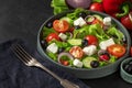 Fresh greek salad with olives, feta cheese, tomato, cucumber, onion with fork on towel on black background