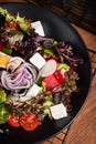 Fresh greek salad with tomato, radish, onion, bel pepper , olives and feta cheese on black plate, top view, wooden background Royalty Free Stock Photo