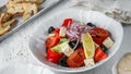 Fresh Greek salad with tomatoes, olives, feta cheese, bell pepper, lemon, onion in bowl on light wooden background. Healthy food,