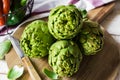 Fresh green artichokes on cutting board top view with peeled off leaves, Italian sweet peppers in basket Royalty Free Stock Photo