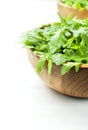 Fresh green arugula leaves on wooden bowl, rucola salad on white wooden rustic background with place for text. Selective focus. Royalty Free Stock Photo