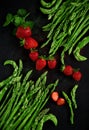 Fresh green asparagus tips with red strawberries decorated beautifully arranged on dark wood plate