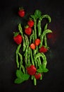 Fresh green asparagus tips with red strawberries decorated beautifully arranged on dark wood plate Royalty Free Stock Photo