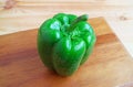 Green bell pepper with water droplets isolated on wooden chopping board Royalty Free Stock Photo