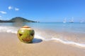 Fresh green coconut with a carved Halloween face.  Lying in the sand on the beach of the sea at sunny day. foam from the wave on Royalty Free Stock Photo