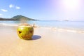 Fresh green coconut with a carved Halloween face.  Lying in the sand on the beach of the sea at sunny day.  Wave on the background Royalty Free Stock Photo