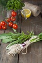 Fresh green garlic spears and arugula on wooden table with tomatoes and lemon