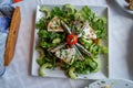 Fresh green lettuce greek mediterranean salad with slice of anchovy, tomato, cheese, cucumber, etc. on white square plate, Mykonos Royalty Free Stock Photo