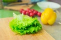 Fresh green lettuce leaves lie on a wooden cutting board next to the yellow bell pepper and red cherry tomatoes on a Royalty Free Stock Photo