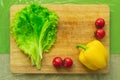 Fresh green lettuce leaves lie on a wooden cutting board next to the yellow bell pepper and red cherry tomatoes on a Royalty Free Stock Photo