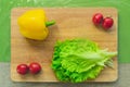 Fresh green lettuce leaves lie on a wooden cutting board next to the yellow bell pepper and red cherry tomatoes on a Royalty Free Stock Photo