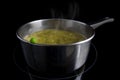 Fresh green pea on a pot with steaming vegetable soup on an induction heater, black background, concept for vitamin-preserving co