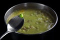 Fresh green pea on a spoon over a pot with dead-boiled soup