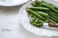 Fresh green peas on a white plate with a wooden spoon, close-up Royalty Free Stock Photo