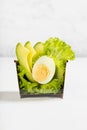 Fresh green salad with green lettuce, avocado, egg in paper box in soft light white bar interior. Concept advertising for delivery Royalty Free Stock Photo