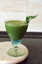 Fresh green smoothie in a wide glass on stem on the kitchen countertop - close up front top view Royalty Free Stock Photo