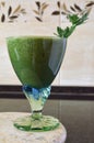 Fresh green smoothie in a wide glass on stem on the kitchen countertop - close up front top view Royalty Free Stock Photo